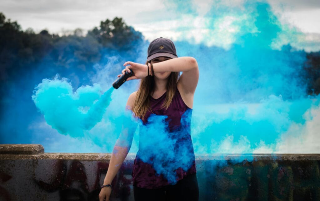 Home 5 A stylish woman surrounded by bright blue smoke outdoors, creating a dynamic fashion statement.