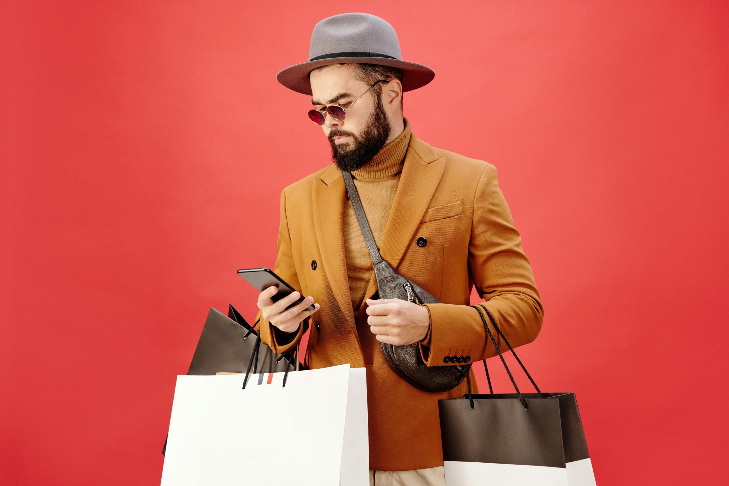 Home 85 Fashionable man with shopping bags using smartphone. Stylish look with beard, hat, and sunglasses.